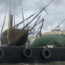 People watch as derelict vessels are loaded onto a barge.