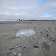Kids on the beach with plastic bottle trash in the foreground.