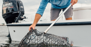 Man leaning over the side of a boat pulling a fish trap up from the water.
