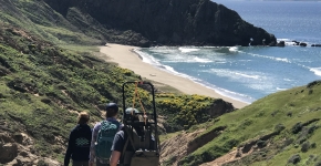 Three people hiking together through hills overlooking an ocean beach.