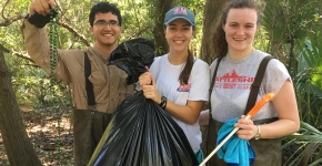 Project participants holding a bag of collected debris as well as collected Mardi Gras beads.