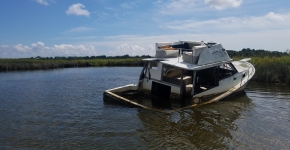 An abandoned and derelict vessel partially submerged and stuck in a marsh.