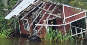 A dilapidated house surrounded by vegetation sinks into a river.
