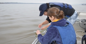 Two people taking a water sample from a boat.