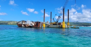 A large vessel sits with its side resting partially underwater with a crane and platform next to it. 