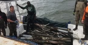 Five volunteers stand in a boat loaded with debris.