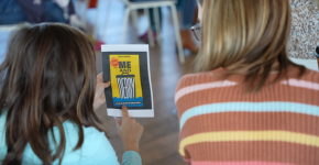 A woman with blond hair and a child with brown hair, seen from behind as they are reading the cover of the playbill for “Me and Debry.” 