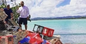 Two men stand on a beach next to a pile of collected crab traps.