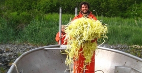 A man dressed in all orange stands in a boat holding a pile of yellow rope.