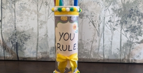 A tall canister decorated and holding a ruler and long straws.