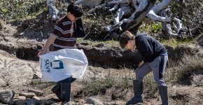 Two students survey for debris among rocks and driftwood. 