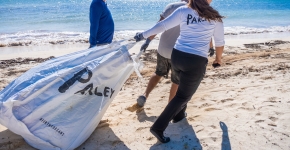 Three people carry a large bag down the beach during a cleanup.