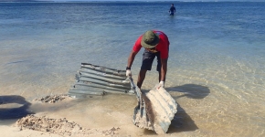 A volunteer removing corrugated roofing tin from an ocean shore.