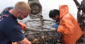 Two people handle a derelict crab pot on a boat.