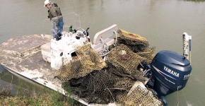 A person stands on a small vessel that is loaded up with derelict fishing traps.