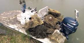 Man standing at the front of his boat with a pile of derelict crab traps piled at the rear.