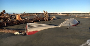 A damaged skiff partially buried in the sand.
