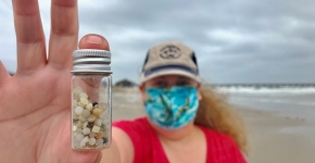 Nurdle Patrol citizen scientist holding up a small jar full of plastic pellets, or nurdles, collected on the beach.
