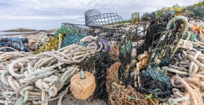 A pile of colorful fishing rope, buoys, and fishing traps are abandoned and sprawled across a coastline with a rocky outcropping in the background.