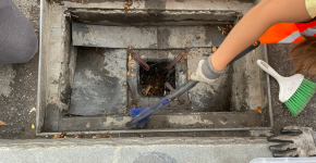 An arm with a brush reaches into a storm drain catch basin to clean it.