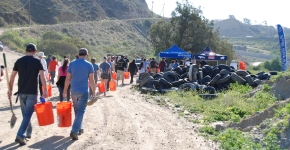 Volunteers with orange buckets walking up a dirt road past a pile of old tires.