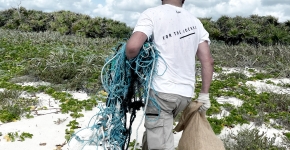 A person on a beach carrying a bag full of debris and a small mass of derelict fishing nets.