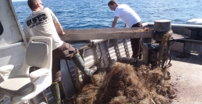 Two people hauling a derelict net onto a boat.