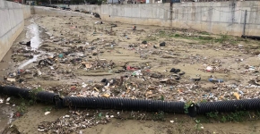 Trash along a muddy riverbed with concrete walls.