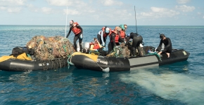 People haul a derelict fishing net into a boat.