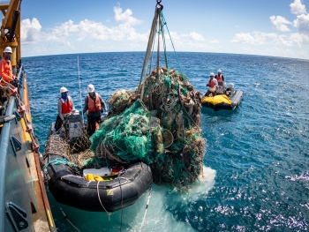 A marine debris removal team member offloads a huge mass of derelict fishing net from a boat.