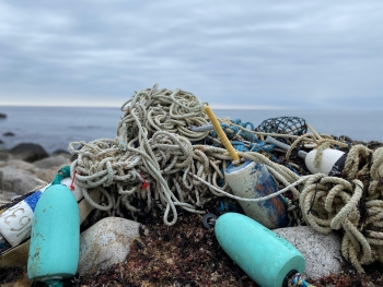 Derelict fishing lines, nets, and buoys piled up on a rocky shoreline.