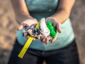 A person holds small debris items collected from Lake Huron in their cupped hands, including food wrappers and a plastic fish.