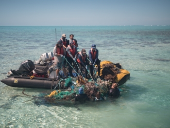 A crew of nine on two small inflatable boats haul a mass of derelict nets out of the water.