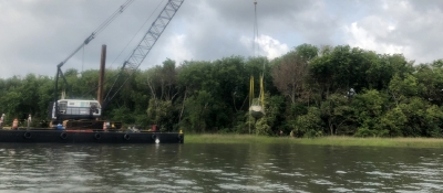 A sailboat being lifted by a crane out of a marsh.