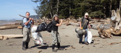 Three people carrying marine debris off a beach.