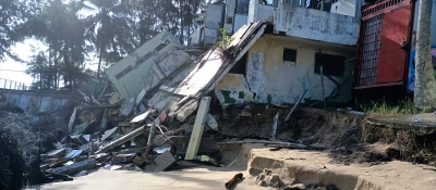 A dilapidated house structure on a tropical, sandy shoreline.