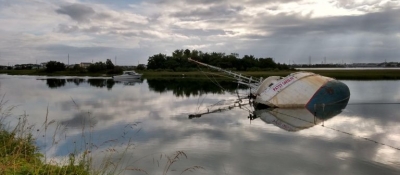 A vessel on its side in a waterway with another vessel passing by in the background.