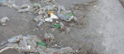 Plastic bottles and other debris litter a shoreline.