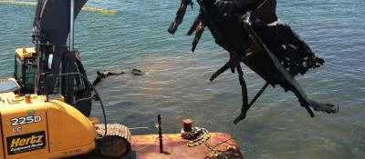 A backhoe lifts pieces of a derelict barge out of the water.