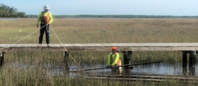 Two people work to remove construction debris from a marsh after a hurricane in Georgia.