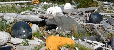 Large pieces of foam and buoys mixed in with natural debris on a shoreline.