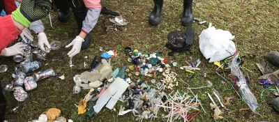 People organize marine debris into piles on the grass.