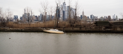 Two abandoned vessels peak out of the water with New York City in the background.