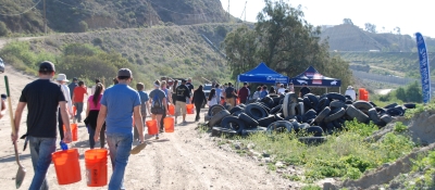 Volunteers carrying buckets and shovels walk toward a large pile of tires.
