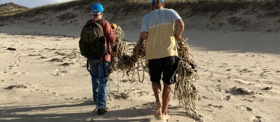 Volunteers removing a large tangle of rope debris from a beach.