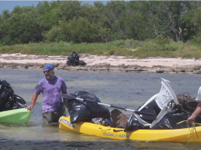 Two people with a canoe clean up garbage from water.