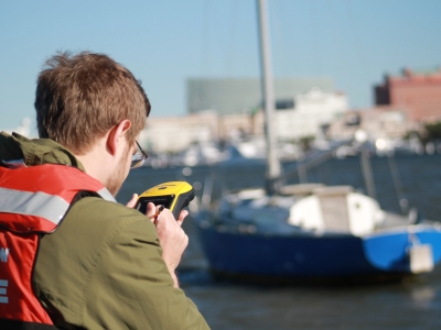 Person near the water and a boat, inputting data on a hand-held device