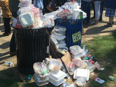 Overflowing trash cans with plastic and styrofoam garbage on the ground.