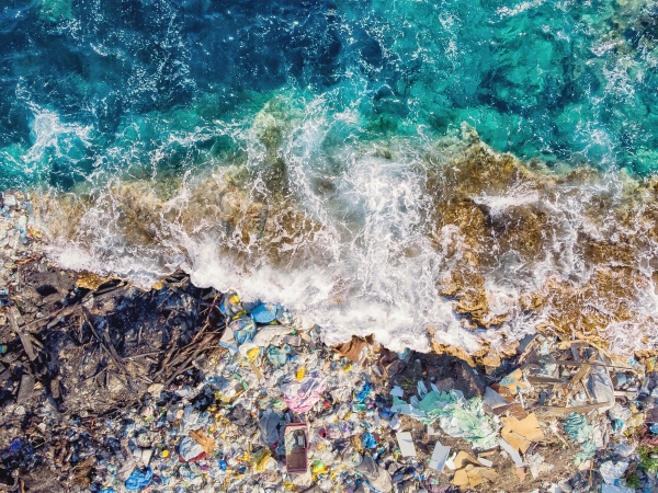 An aerial photograph of a wave crashing on a shoreline that is filled with marine debris.