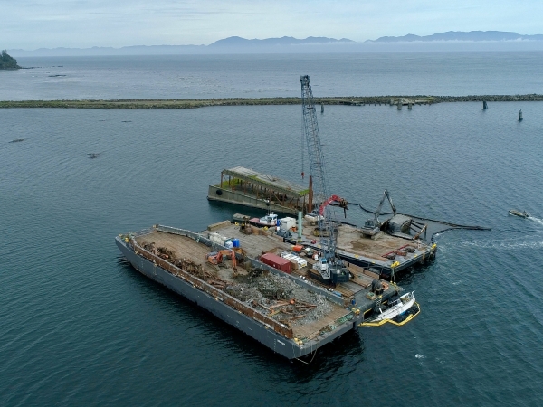 Three barges being used to remove a derelict bridge that sits in a bay.